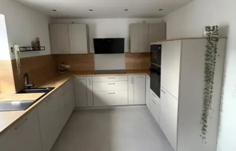 Moderne Küche mit weißen Schränken, einer Küchenrückwand aus Holz, Einbaugeräten, einer untergebauten Spüle, einem Elektrokochfeld sowie kleinen Pflanzen auf der Arbeitsplatte und den Regalen.