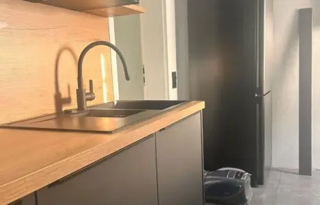 Eine Küche mit einer Arbeitsplatte in Holzoptik, einer schwarzen Spüle, einer mattschwarzen Armatur und einem schwarzen Kühlschrank. Eine Küche mit einer Arbeitsplatte in Holzoptik, einer schwarzen Spüle, einer mattschwarzen Armatur und einem schwarzen Kühlschrank.