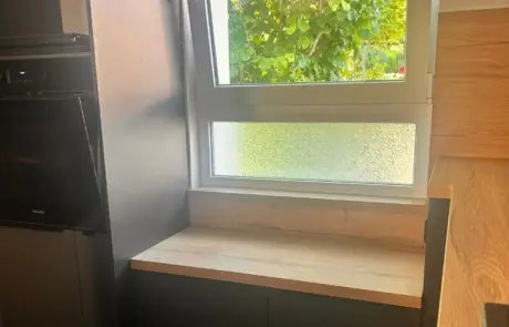 Eine Arbeitsplatte aus Holz, die in einer Küchenecke unter einem zweiflügeligen Fenster eingebaut ist. Eine Arbeitsplatte aus Holz, die in einer Küchenecke unter einem zweiflügeligen Fenster eingebaut ist.